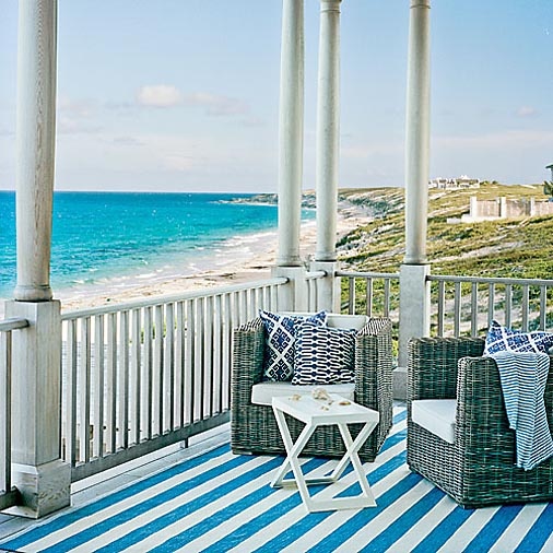 a beach patio with a couple of wicker chairs and a trestle table, printed textiles and a beautiful sea view