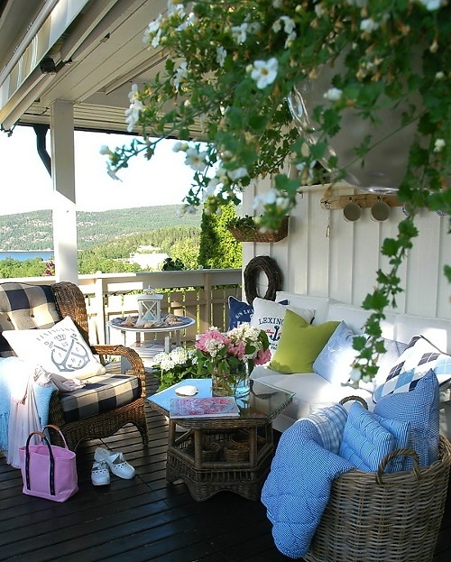 a rustic sea porch with wicker furniture, a bench with white upholstery, bright textiles and potted plants and blooms