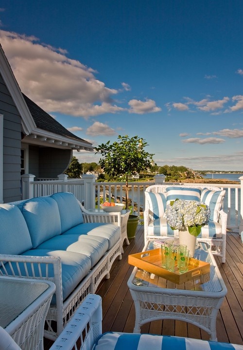 a beach porch with white wicker furniture, blue upholstery, potted plants and blooms and a beautiful sea view