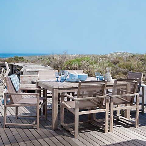a neutral wooden beach patio with simple furniture, blue tableware and a fantastic sea view