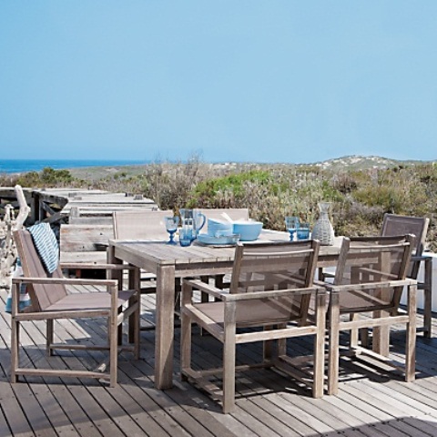 a neutral wooden beach patio with simple furniture, blue tableware and a fantastic sea view