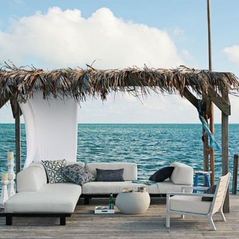 a seaside terrace with neutral upholstered furniture, printed and black pillows and a small roof with grasses