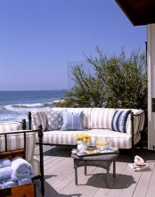 a beachy terrace with a wooden deck, black forged furniture, striped upholstery, a vintage coffee table and a fabulous sea view