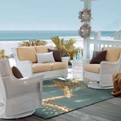 a bright beach terrace with white wicker furniture, neutral upholstery, a printed rug and a beautiful sea view