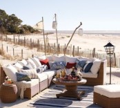 a beach patio with wicker furniture, white upholstery and bright pillows, candle lanterns and a striped rug