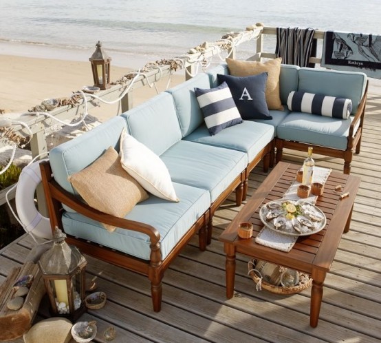 a beach patio with rich-stained wooden furniture and blue upholstery, striped pillows, candle lanterns and seashells and rope for decor