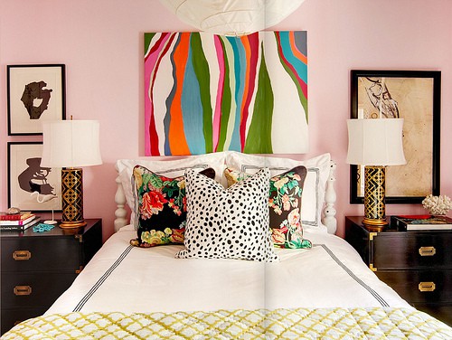 an elegant pink bedroom with a super bright artwork, black nightstands and table lamps, colorful pillows and bedding is amazing