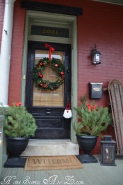 traditional Christmas porch decor with mini Christmas trees, a lantern, a wreath with red ornaments and a red bow