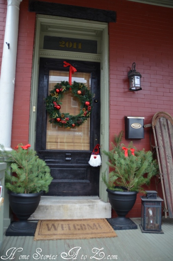 traditional Christmas porch decor with mini Christmas trees, a lantern, a wreath with red ornaments and a red bow