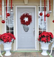 a bright Christmas porch with red and silver ornaments hanging down and poinsettia arrangements plus a red berry wreath on the door is bright and cool
