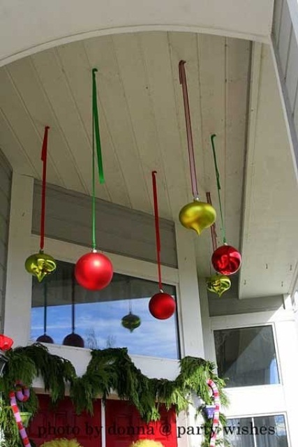 colorful Christmas ornaments hanging over the porch and an evergreen garland to frame the door make up a colorful Christmas porch