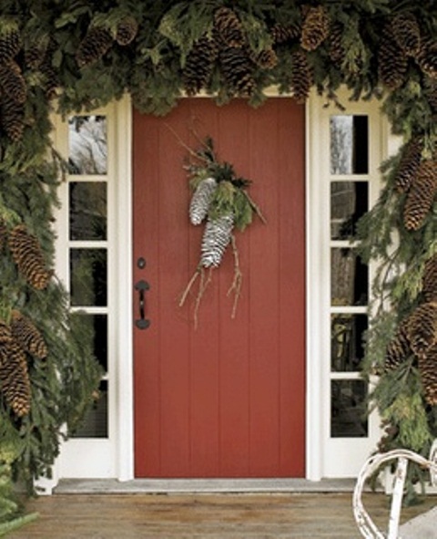 a woodland Christmas porch with a lush evergreen garland with pinecones and some pinecones on the door for a wow effect
