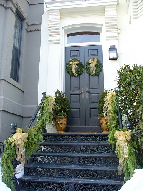 a southern Christmas porch with mini trees, greenery wreaths with bows, greenery garlands lining up the rails and neutral bows