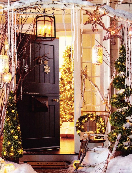 a fairy-tale Christmas porch with branches with snowflakes, a candle lantern, icicles, lit up trees and a lit up wreath is adorable