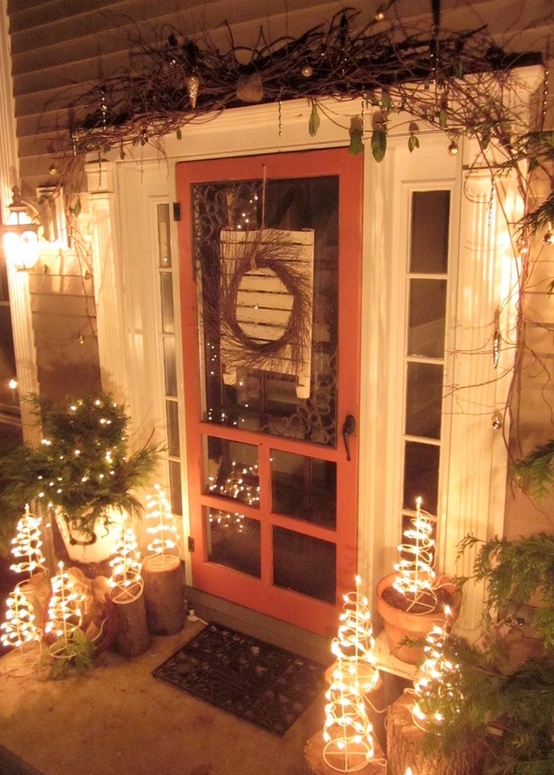 a lit up Christmas porch with vine and hangings, trees of lights, mini Christmas trees with lights is a very boho idea