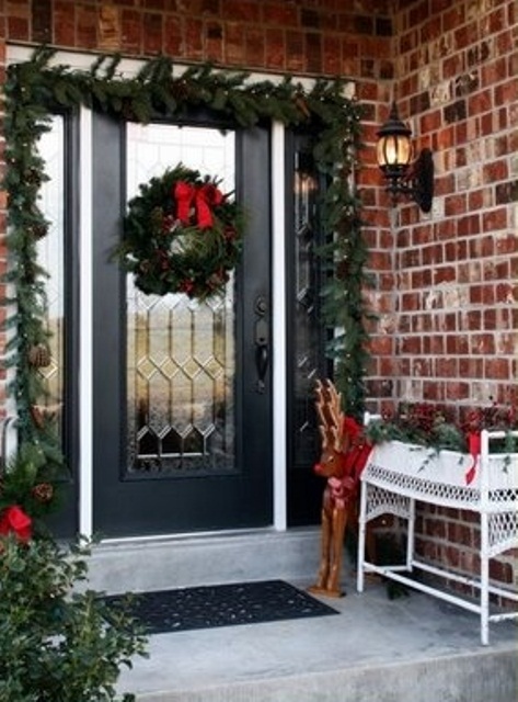 a cozy Christmas porch with an evergreen garland with lights over the door, a greenery wreath with a red bow, evergreens and red ribbons, greenery with a red bow