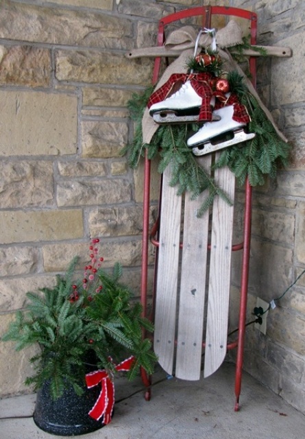 a vintage sleigh with a burlap bow, fir branches, skates and red bells plus an evergreen arrangement with red berries and a bow