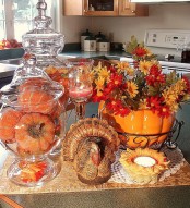 faux orange pumpkins in a glass jar, a bright pumpkin pot with fall blooms and a porcelain figurine