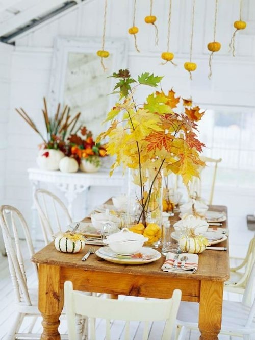 a tablescape spruced up with a lush fall leaf arrangement, pumpkins and some pumpkins hanging over the table