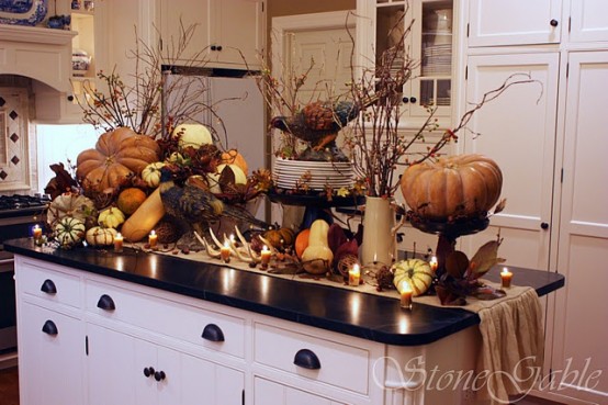 a kitchen island decorated with oversized faux pumpkins, gourds, antlers, branches, berries and figurines