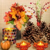 large pinecones, candles in fall candleholders, a faux pumpkin and an arrangement of fall leaves