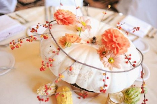 a fall centerpiece of a large white pumpkins, berries and orange blooms is ideal for fall party decor