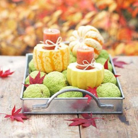 a metal tray with green balls, faux pumpkins with red candles inserted is a stylish fall party centerpiece idea