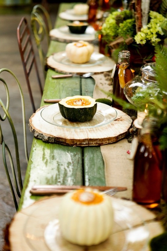 a natural fall tablescape with an uncovered table, natural pumpkins, greenery arrangements and wood slices instead of placemats