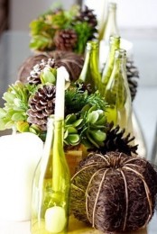 a fall centerpiece of pinecones, vine and usual white pumpkins, candles, greenery and green bottles