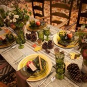 a stylish fall party tablescape with green glasses and plates, gold chargers and cutlery, pincones, fall leaves and fall floral arrangements