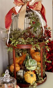 a cage filled with real pumpkins and gourds and topped with a ribbon bow for natural fall decor