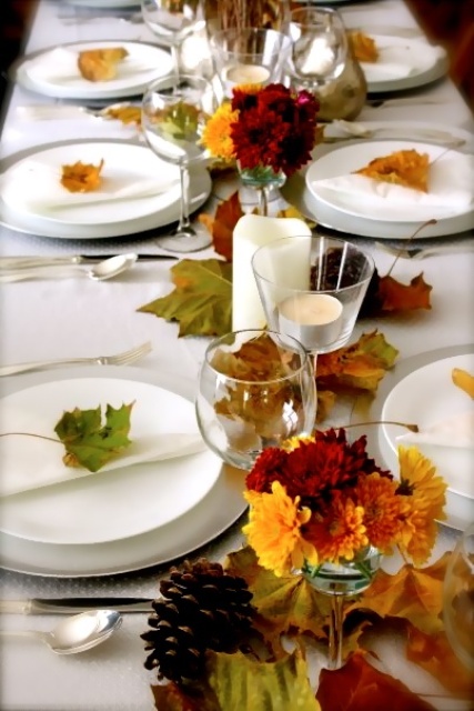a neutral fall tablescape with bright fall leaves, candles and pinecones looks very natural and very modern