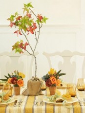 a bright fall tablescape with a plaid tablecloth, bright floral centerpiece and a fall tree in burlap plus mustard glasses