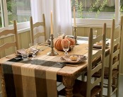a neutral fall table setting with a plaid tablecloth, natural pumpkins and candles plus printed porcelain