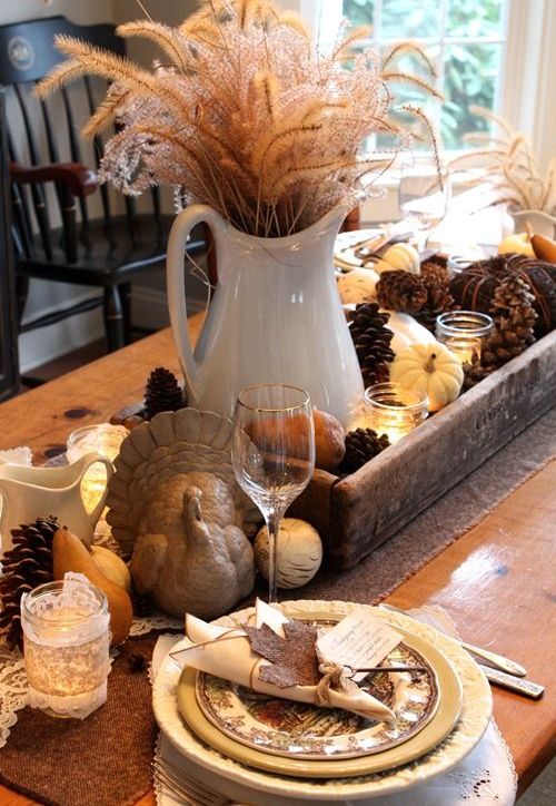 a rustic fall tablescape with pinecones, pumpkins, candles and a wheat arrangement plus porcelain plates