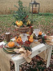 a vintage-inspired fall table setting with a burlap runner, printed plates, candles, faux pumpkins, berries, a vintage urn with greenery, pumpkins and berries