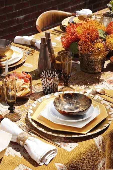 a bright fall table setting with a mustard tablecloth, layered colorful plates and a bold protea centerpiece