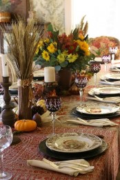 a vintage-inspired tablescape with a printed tablecloth, faux pumpkins, pinecones, wheat and floral arrangements and printed plates