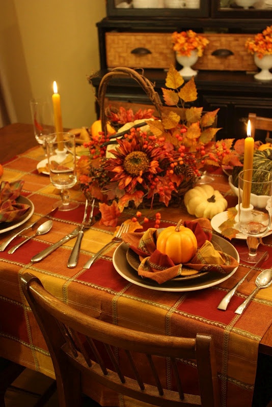 a bright fall tablescape with a plaid tablecloth and napkins, tall candles, fall leaves and berries in a basket