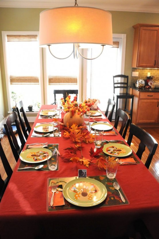 a colorful fall tablescape with bright textiles, fall leaves and a pumpkin that holds skewers with fruits and veggies
