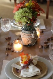 a natural fall table setting with a bright floral arrangement, nuts, candles, a napkin with a fall leaf and ribbons