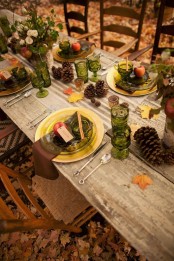 a fall tablescape with pinecones, fall leaves, apples, green glasses and florals plus gold chargers