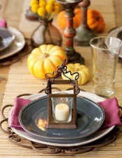 a colorful fall table setting with a purple napkin, a candle mini lantern, faux pumpkins and a woven table runner