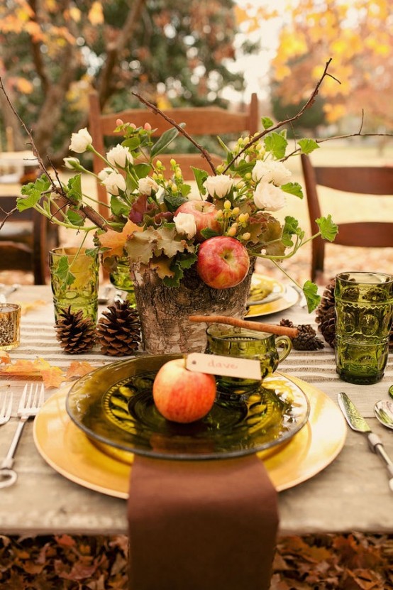 a lush fall tablescape with green glasses and plates, with pinecones, gold chargers, cinnamon sticks and apples looks very natural