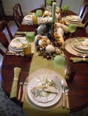 a cozy fall tablescape in neutrals and green, with green glasses and candles, natural pumpkins, nuts and acorns