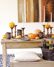 a fall table setting with tall candles, natural pumpkins, elegant candleholders and a bamboo table runner