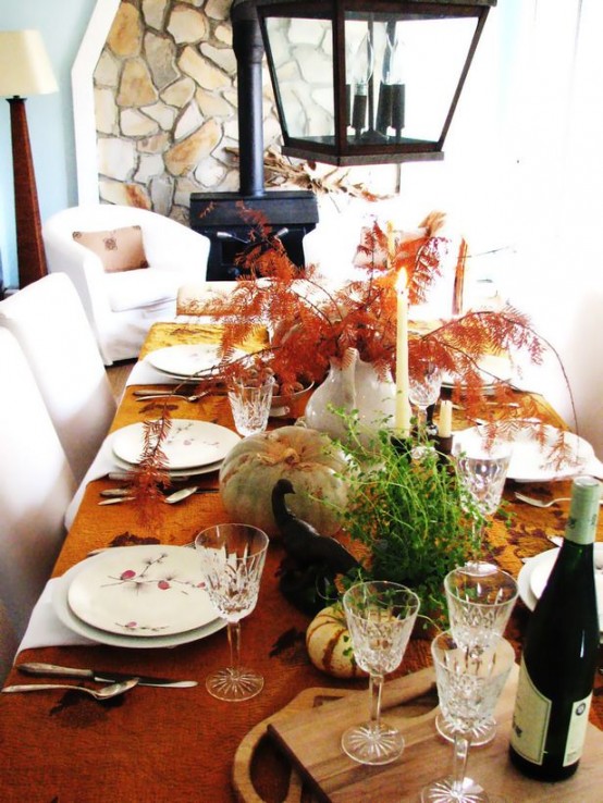 a bold fall tablescape with a rust-colored tablecloth, natural pumpkins and greenery, tall candles