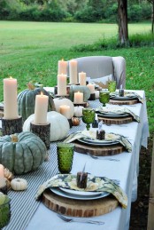 a natural fall tablescape with a striped table runner, heirloom pumpkins and candles on tree stumps