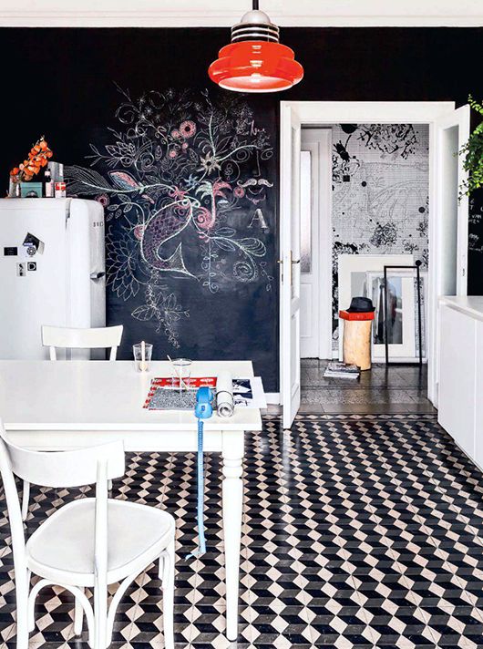 a Scandinavian kitchen with a chalkboard wall, a black and white geo tile floor, white furniture and a red pendant lamp