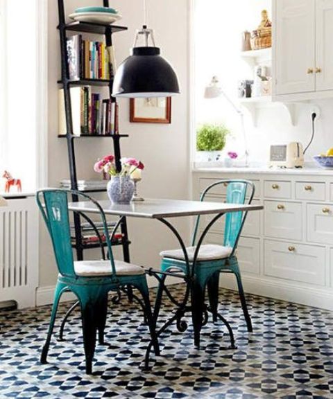 a modern kitchen with white cabinets, a black ladder for storage, a geometric tiled floor, a wooden table and metal chairs in turquoise and black